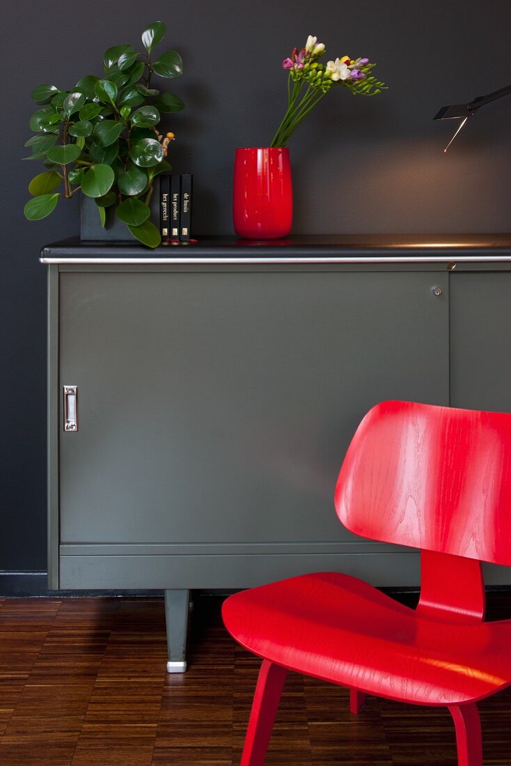 Red classic chair in front of grey designer sideboard against black wall