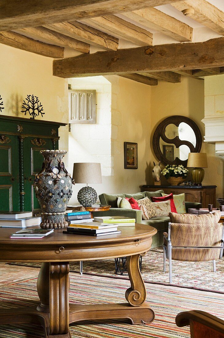 Antiker, runder Holztisch vor Loungebereich in mediterranem Landhaus mit Holzbalkendecke