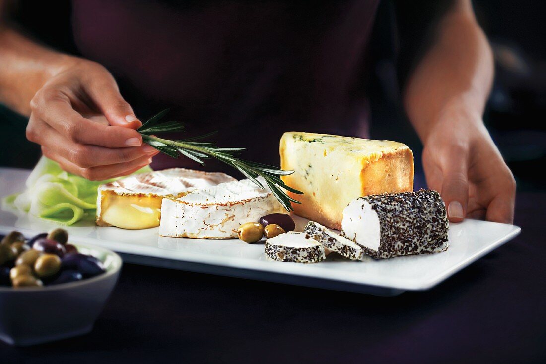 A cheese platter with olives and rosemary sprigs