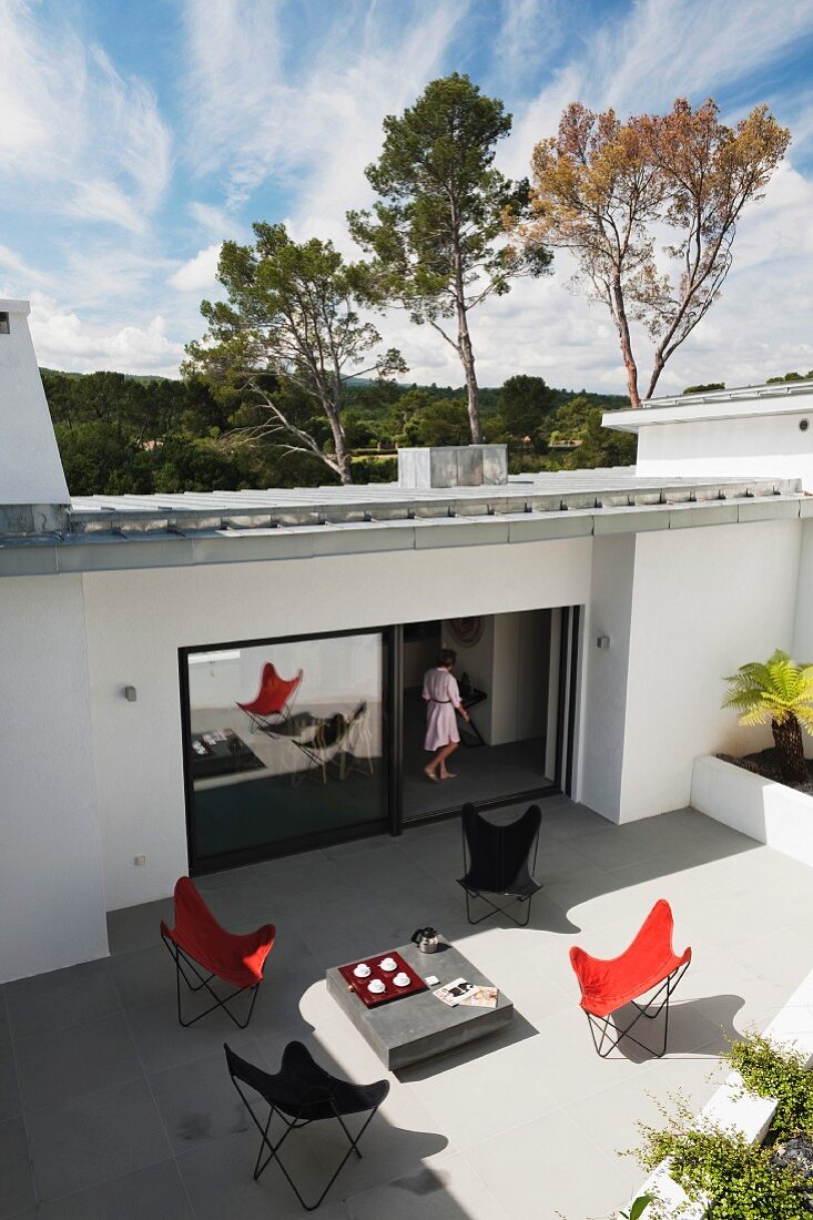 Butterfly armchairs in various colours on large terrace of modern house with woman standing in open terrace door