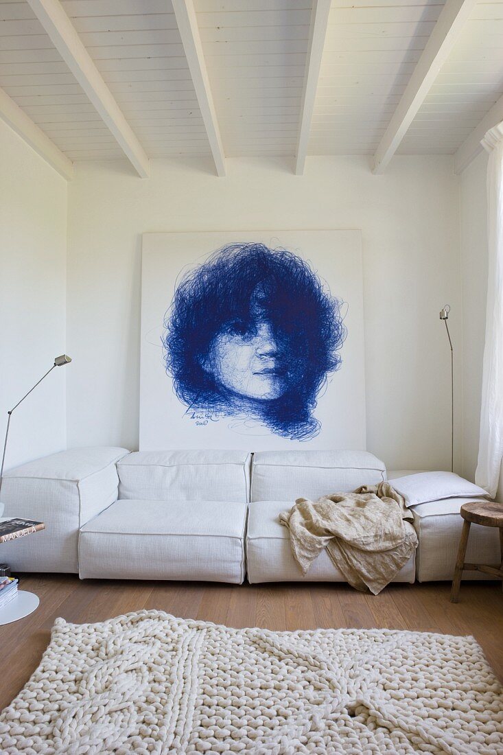 Living room with a white rug and couch upholstered in light fabric in front of a wall with a portrait drawing