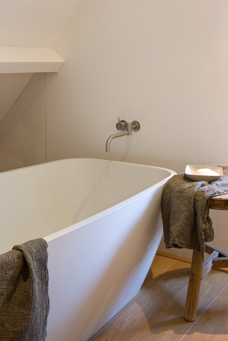 Modern bathtub with a wall mount tub faucet and wooden stool