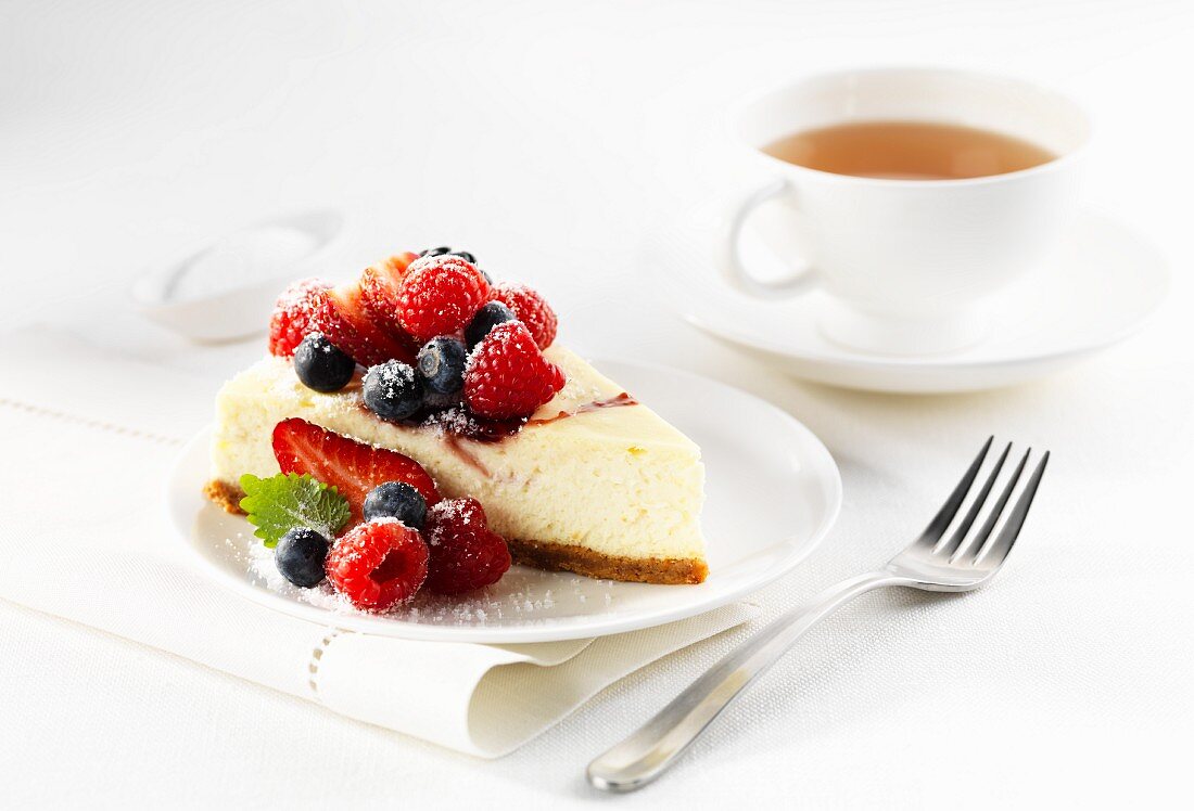 A slice of cheesecake with berries and a cup of tea