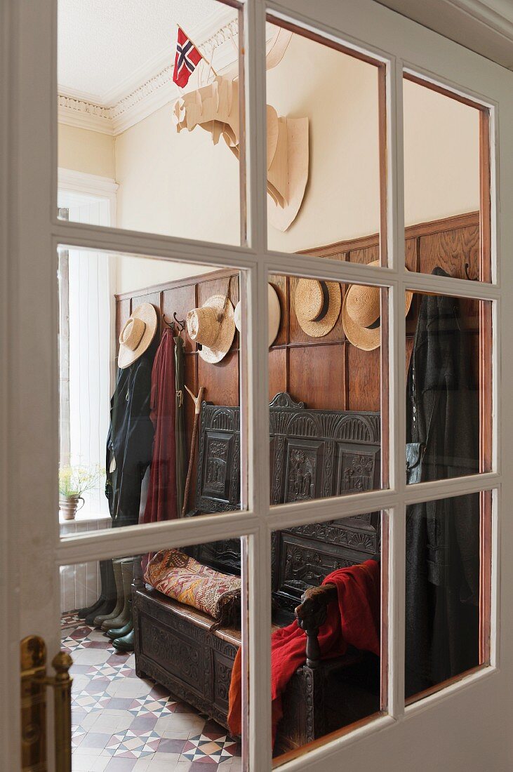 Blick in gefliesten Eingangsbereich mit großer Garderobe und einer antiken Sitzbank mit hoher Rückenlehne