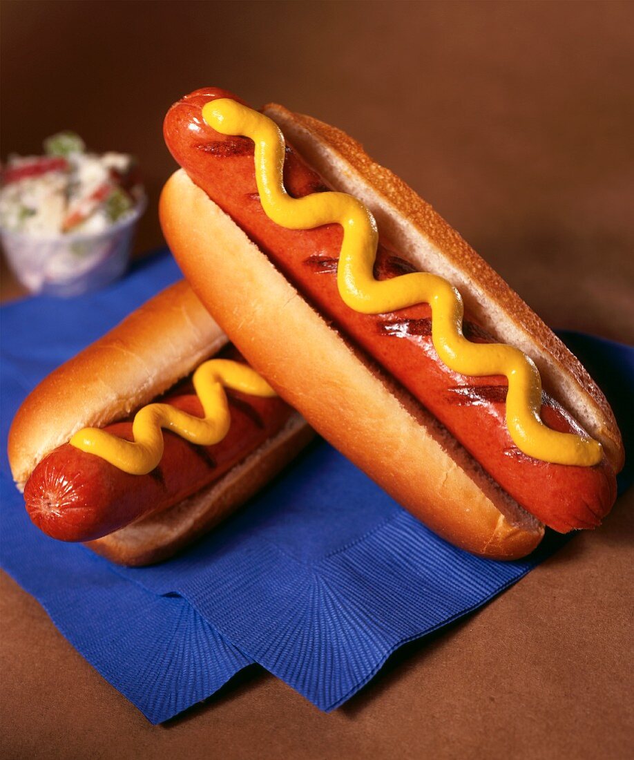 Zwei Hot Dogs mt Senf auf blauen Servietten