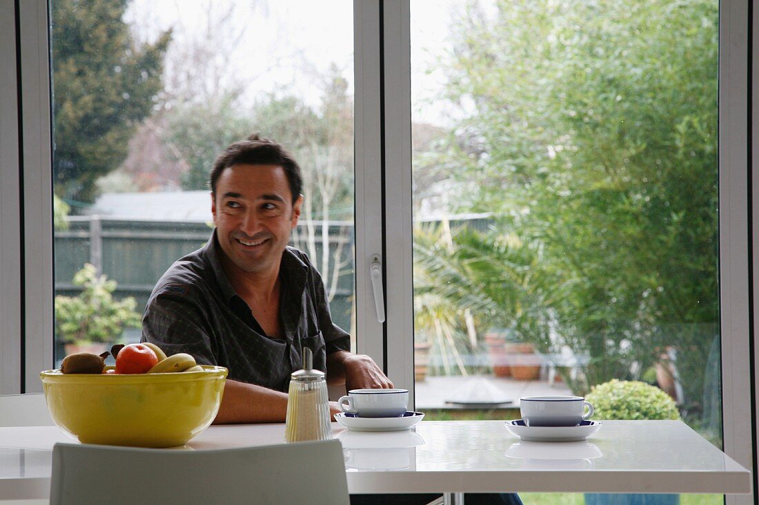 Man having a coffee break at a modern table in front of terrace windows