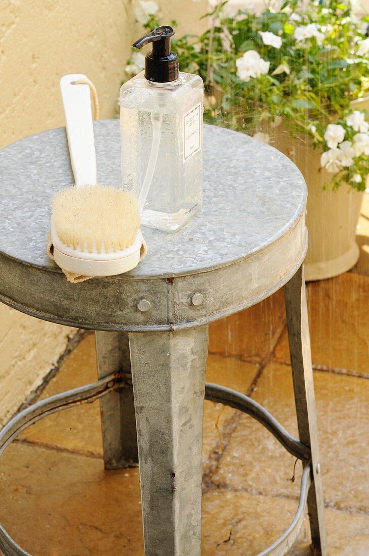 Shower gel and a back brush on a zinc stool beneath the garden shower