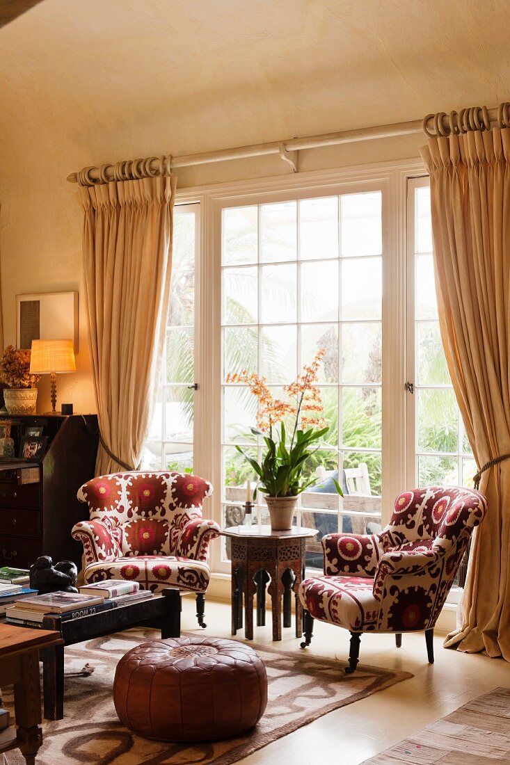 Pair of matching armchairs upholstered in Kathryn Ireland fabric and moroccan leather pouffe in living room with coved ceiling