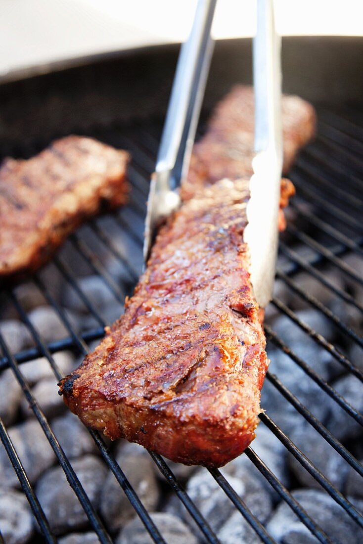 Tongs Flipping Grilled Argentinian Steak on Charcoal Grill