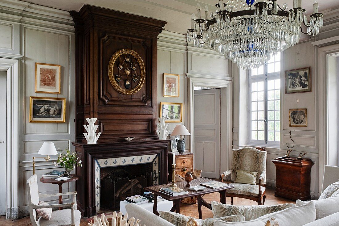 Crystal chandelier above lounge area and fireplace with wood-panelled chimney breast in grand living room