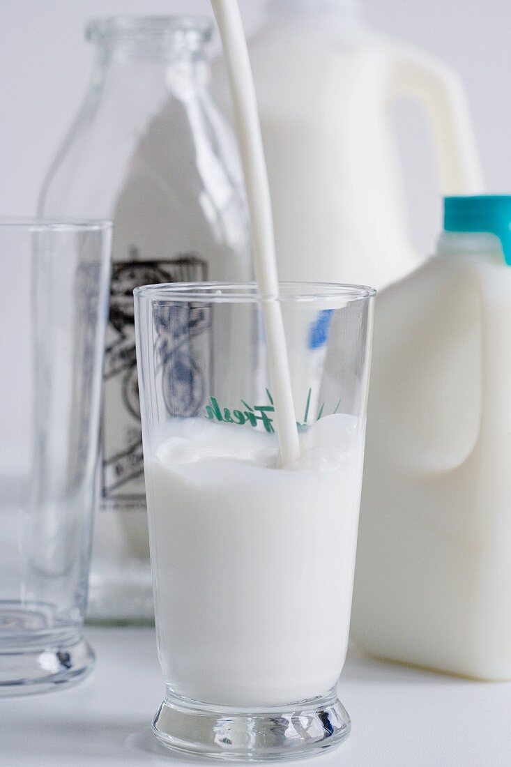 Milch in Glas gießen, Milchflaschen und leeres Glas