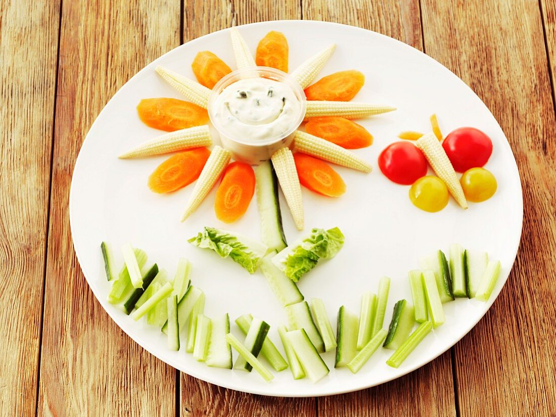 Raw vegetables (cucumbers, carrots, baby corn cobs and tomatoes) and a herb quark dip arranged as a flower and a butterfly on a plate