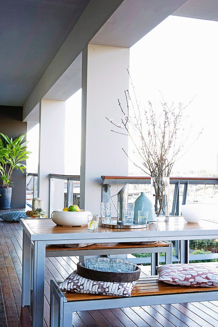 Dining area with light outdoor furniture on elongated terrace loggia with massive facade pillars and parquet floor