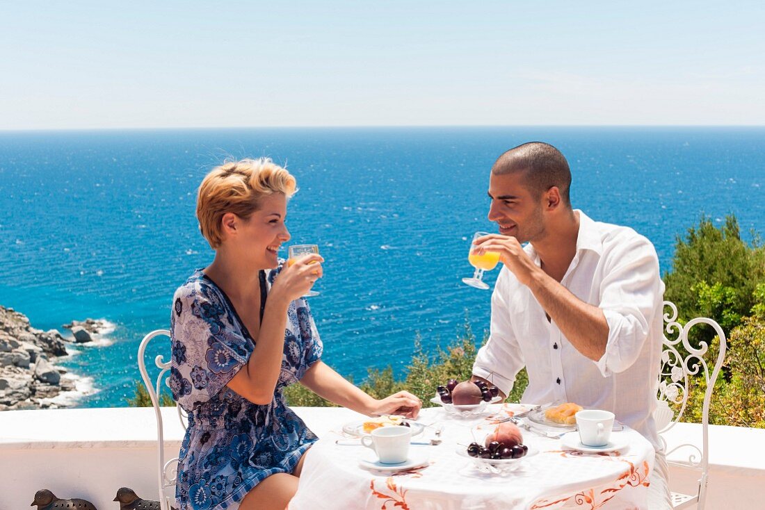 Paar frühstückt auf Terrasse mit Meerblick