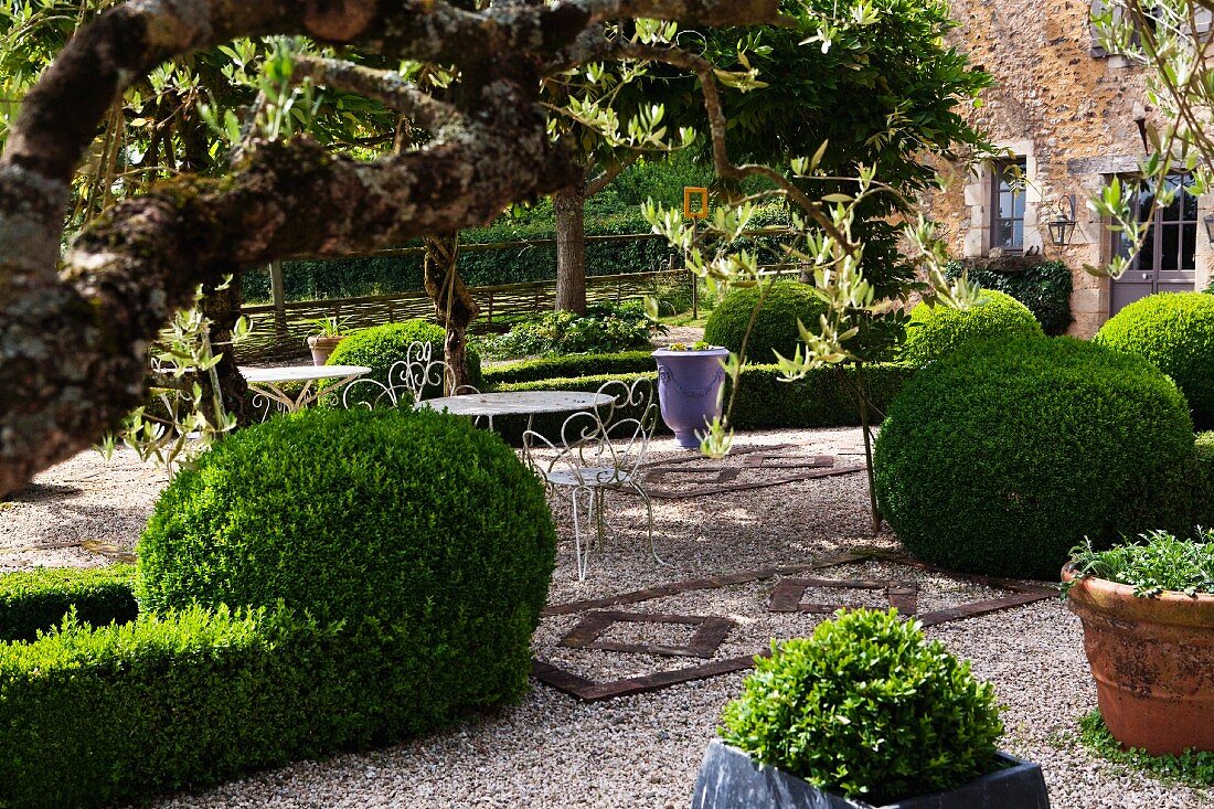 Garden table and chairs on gravel amongst topiary bushes and hedges