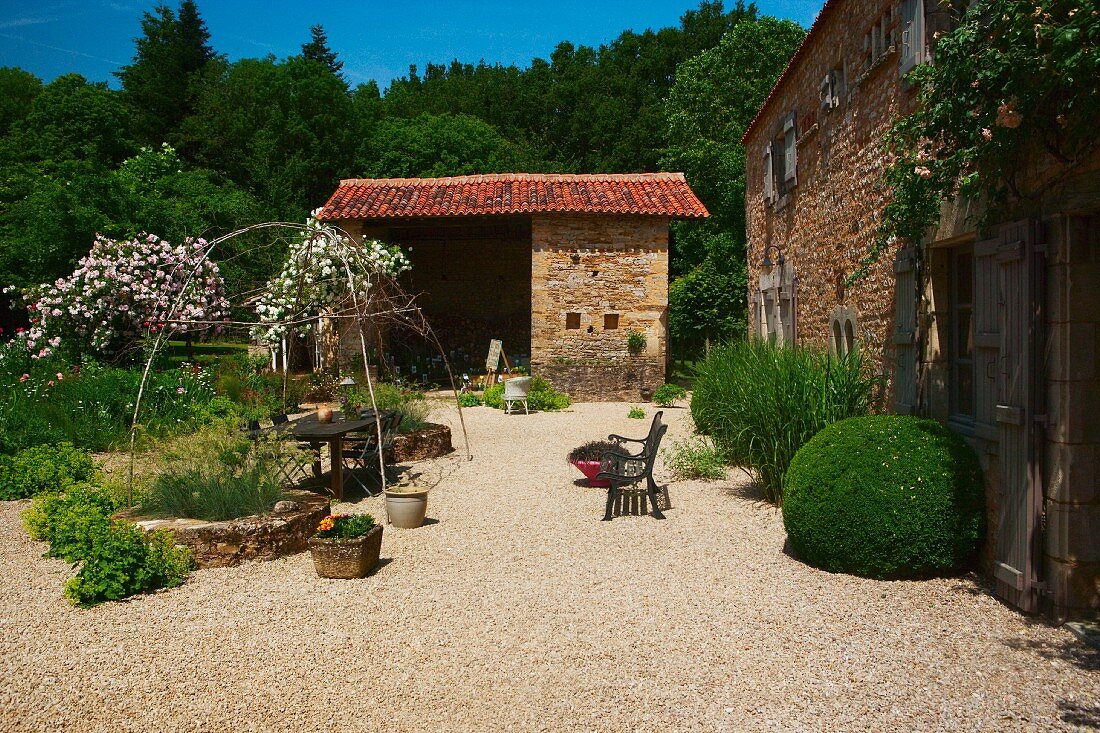 Simple country house and barn in open Mediterranean garden with seating area on gravel terrace