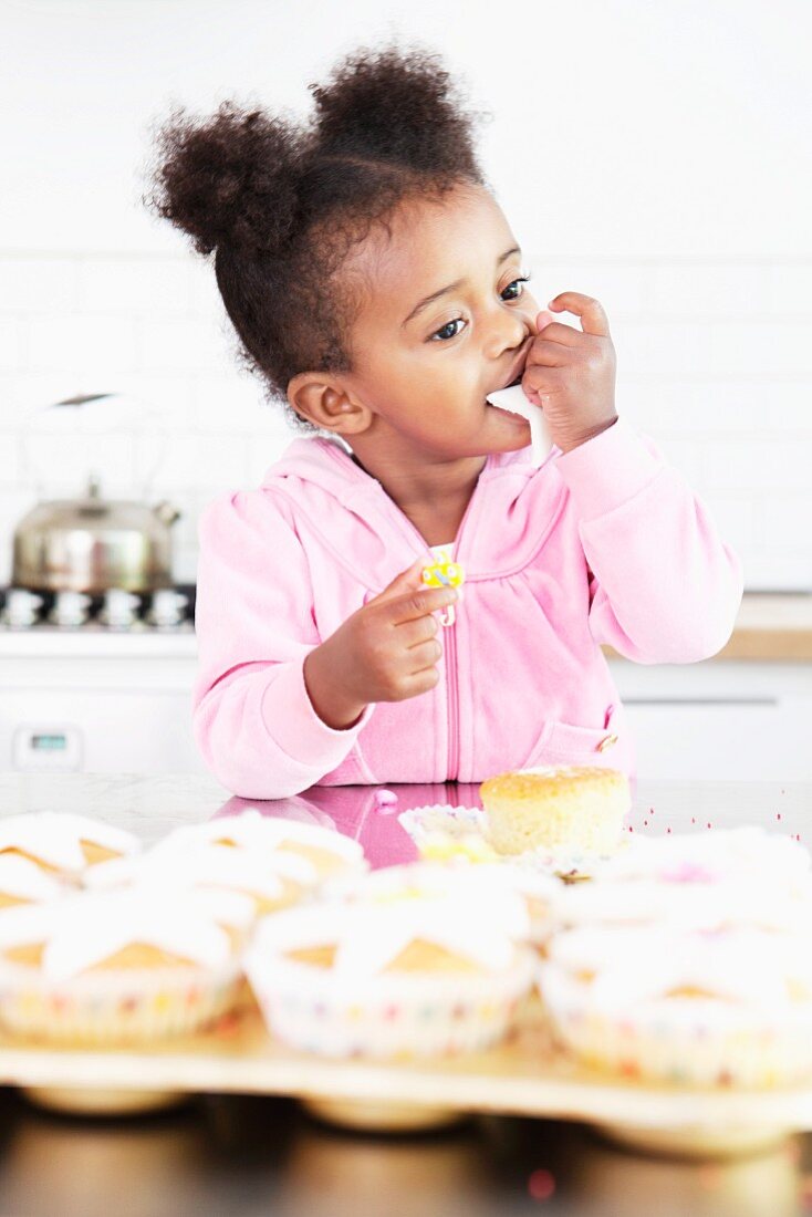A little girl eating frosting from cupcakes