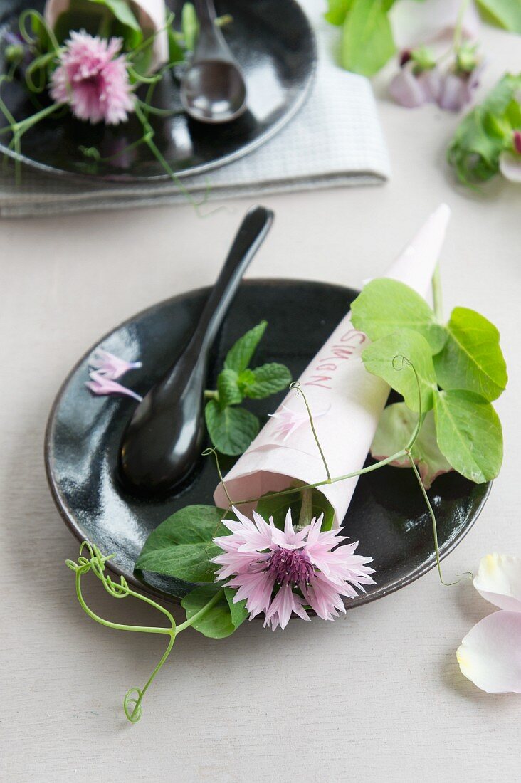 Table setting with a paper cone with a signature filled with corn flowers and trailing vetch