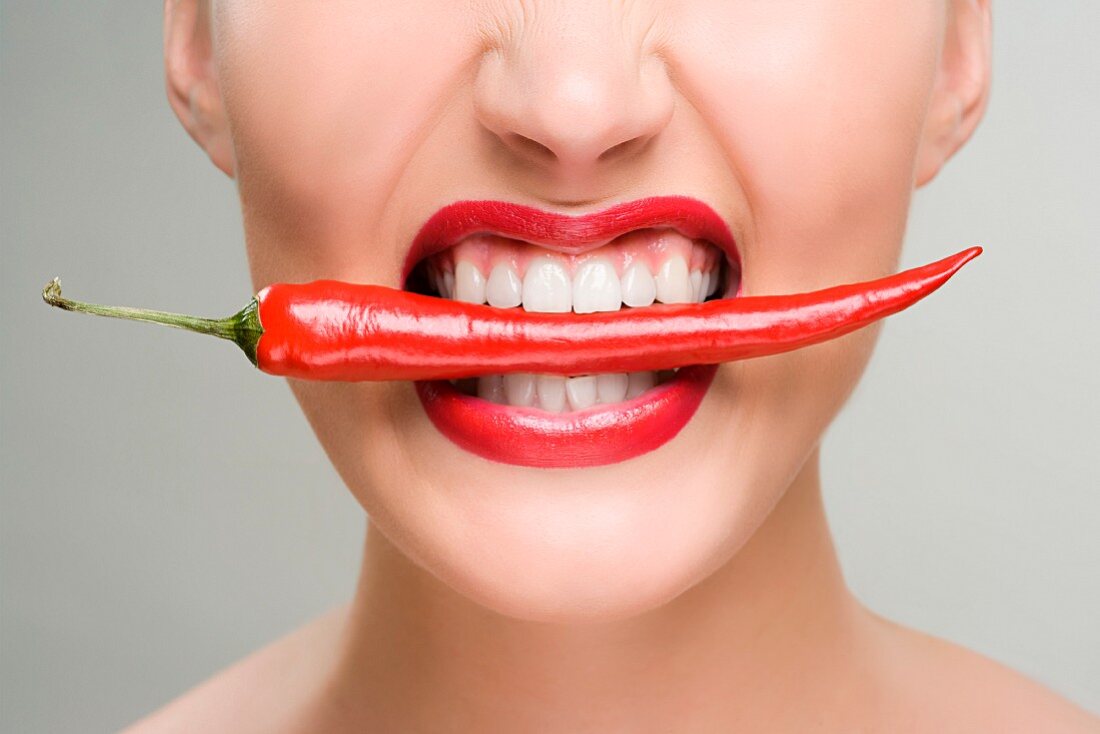 Woman with a red chili pepper between her teeth
