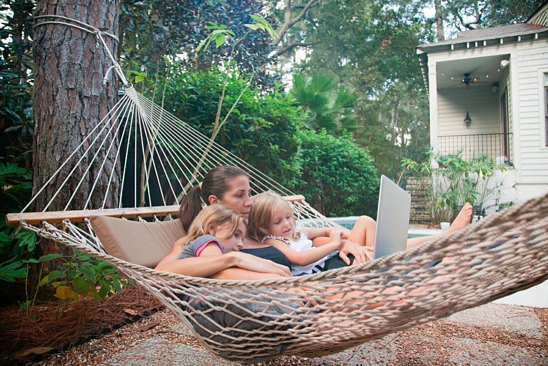 Mother and daughters on hammock with laptop