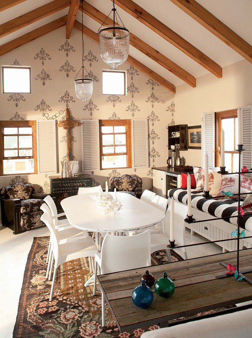weiße Stühle am Esstisch und Sitzbank vor Fenster in offenem Wohnraum unter dem Dach mit Holzbalkendecke