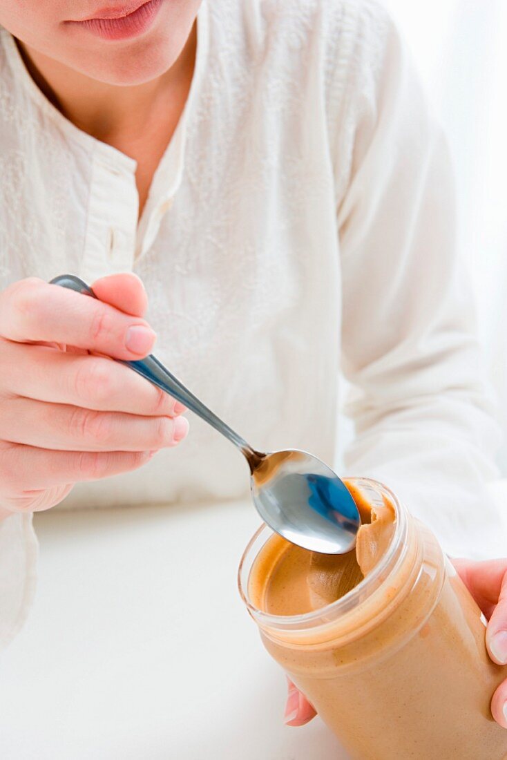 Frau isst Erdnussbutter aus dem Glas