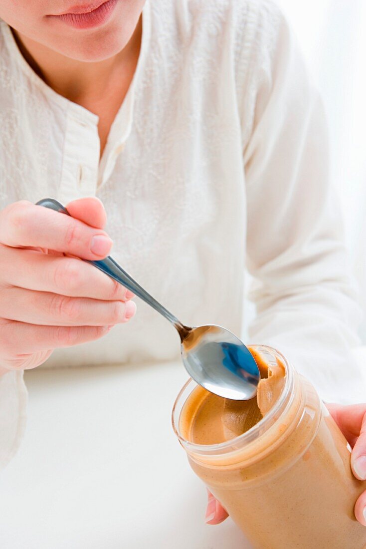 Woman scooping peanut butter from jar
