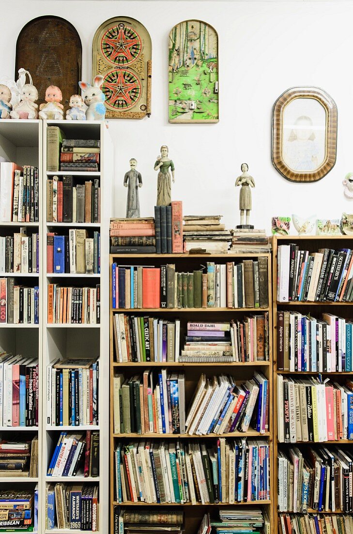 Ornaments standing on books on bookcases of different heights below decorations on wall