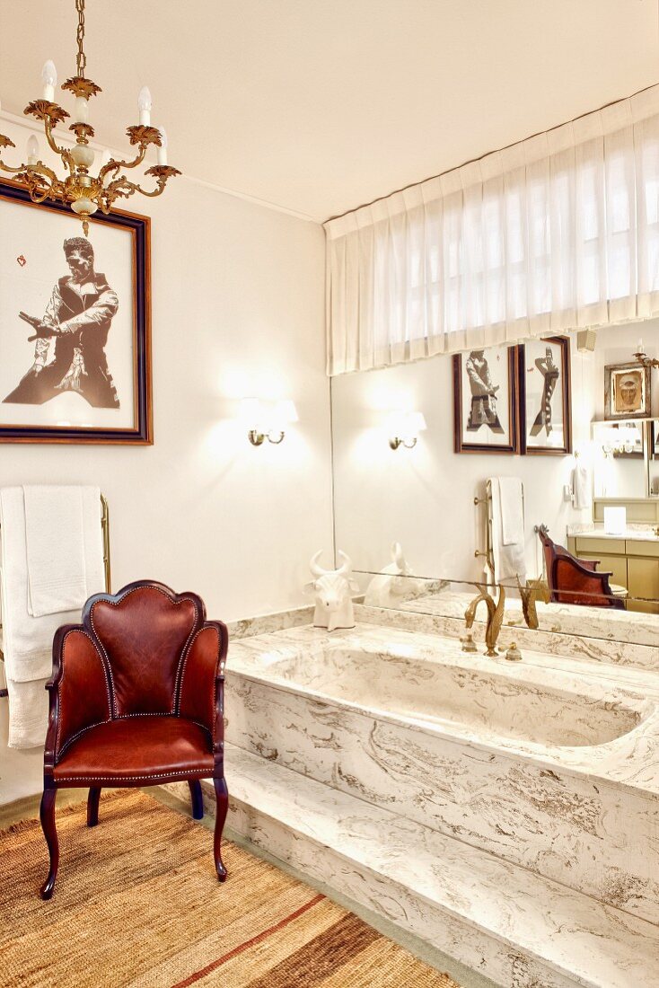 Vintage leather chair next to raised bathtub with step made from marble-style stone