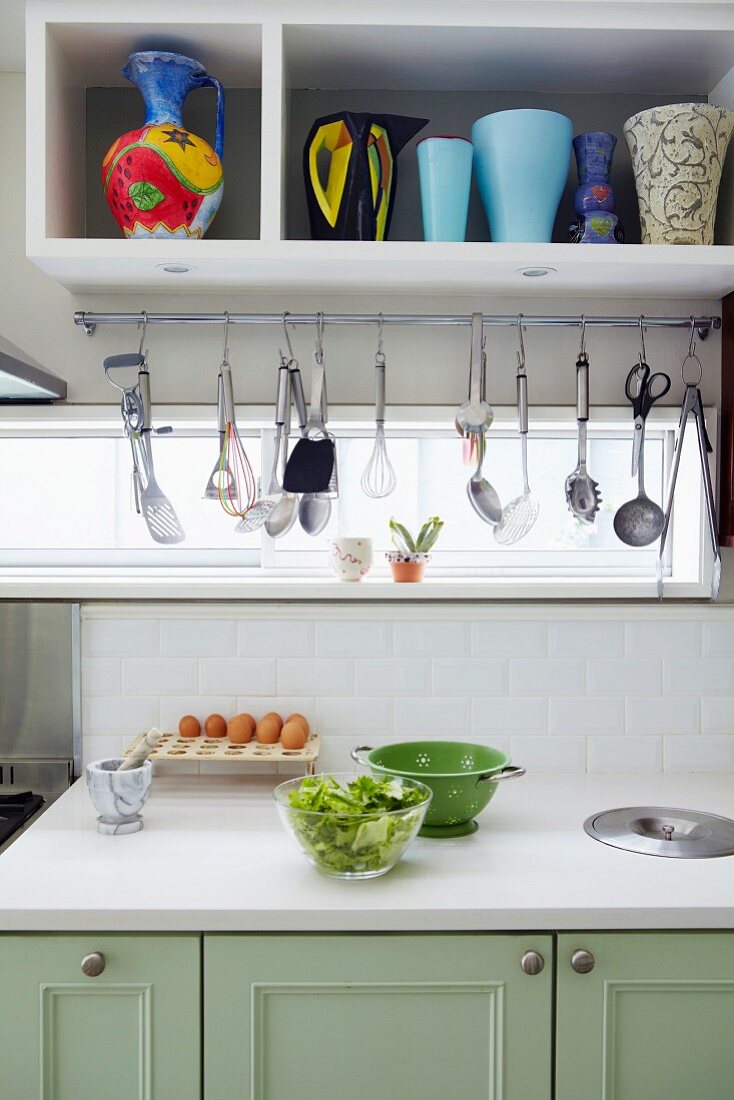 Food preparation on kitchen counter and cooking utensils hanging below wall unit with shelf of vases