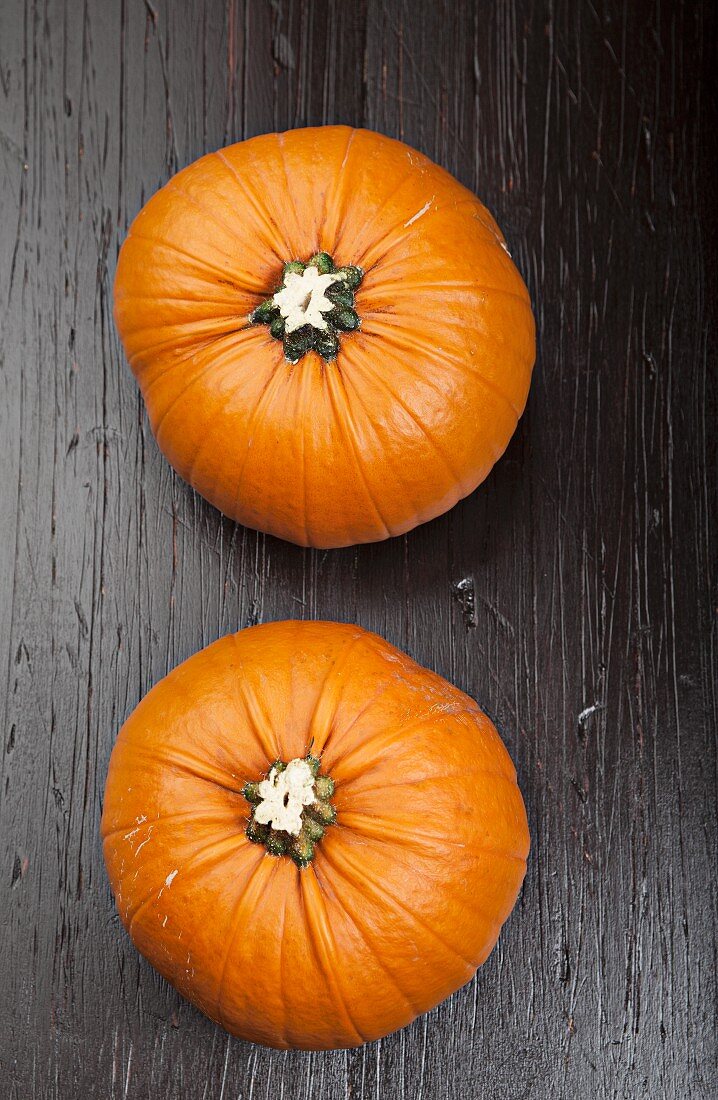 Two orange pumpkins on a wooden surface