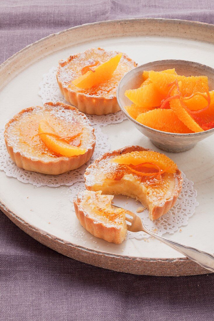 Three orange custard tarts and orange segments on a round tray