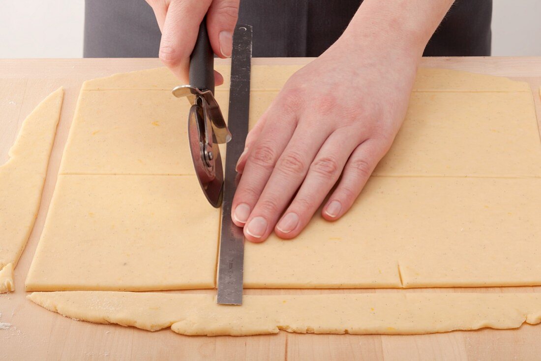 Squares of dough being cut out with a rule and a pizza wheel