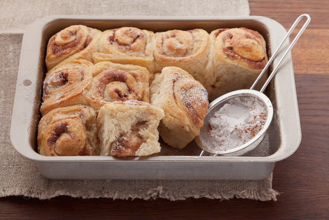 Cinnamon whirls with icing sugar in a baking tin