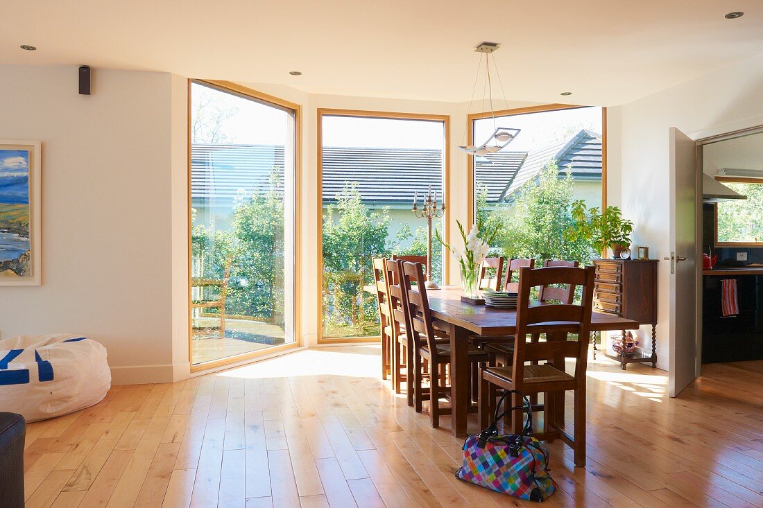 Sunny, spacious dining room with three floor-to-ceiling windows, parquet floor, dining table and solid wooden chairs