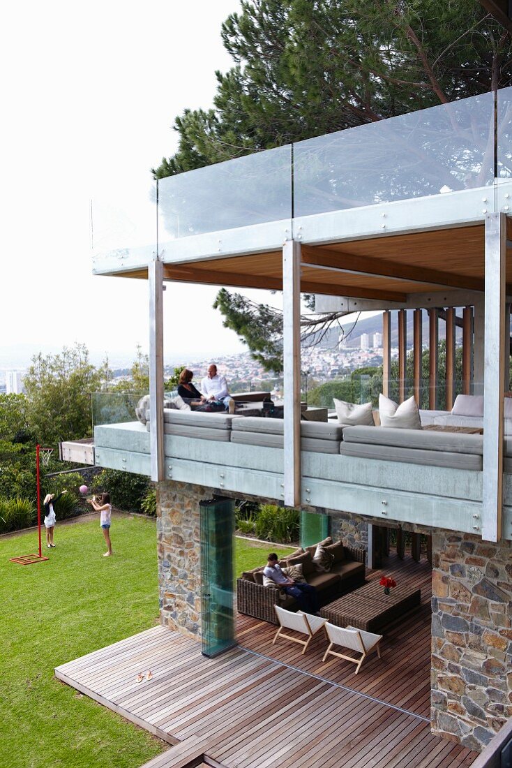 Contemporary residential house with glazed seating area on two storeys; smooth transition between interior floor and wooden terrace