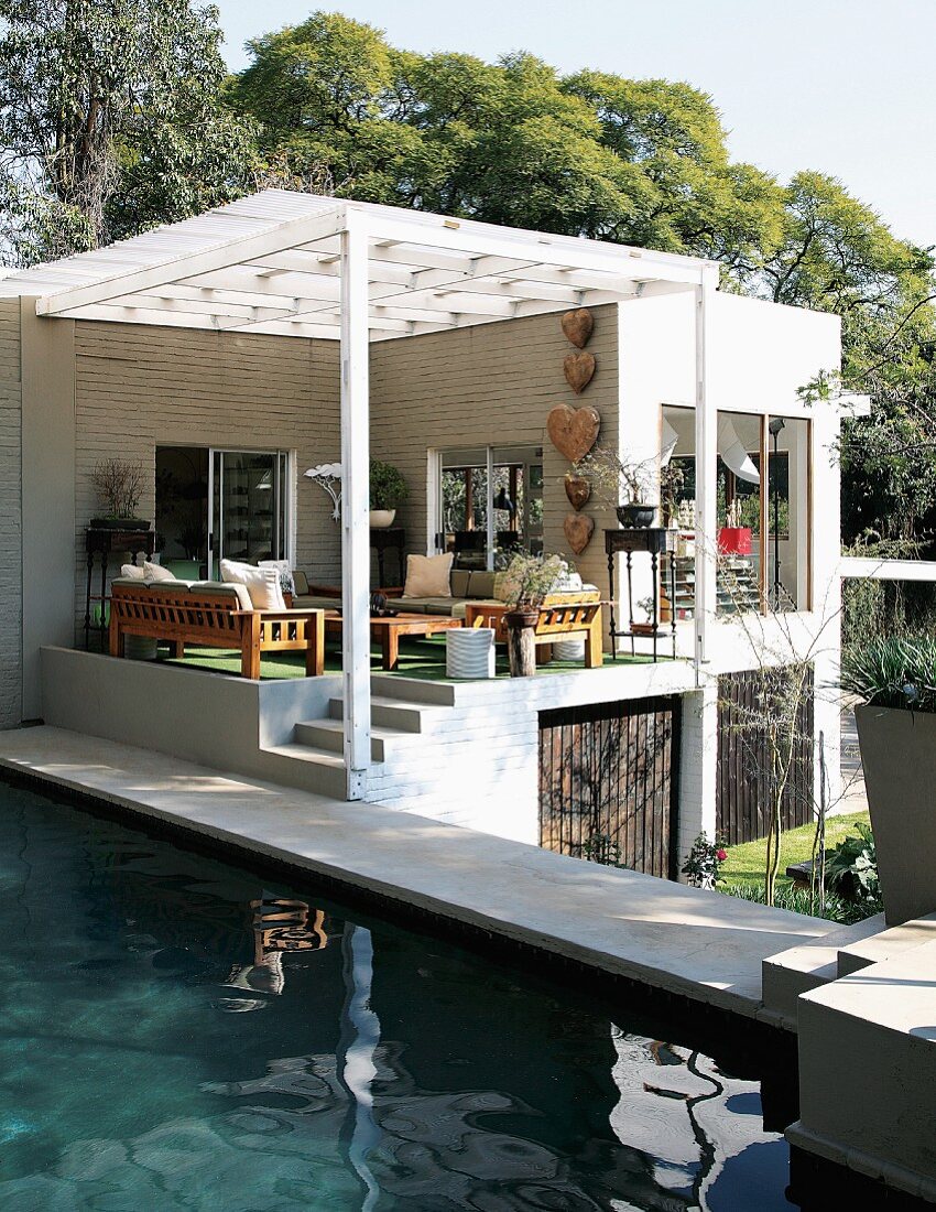 Pool next to contemporary house with roofed terrace in terrain on two levels