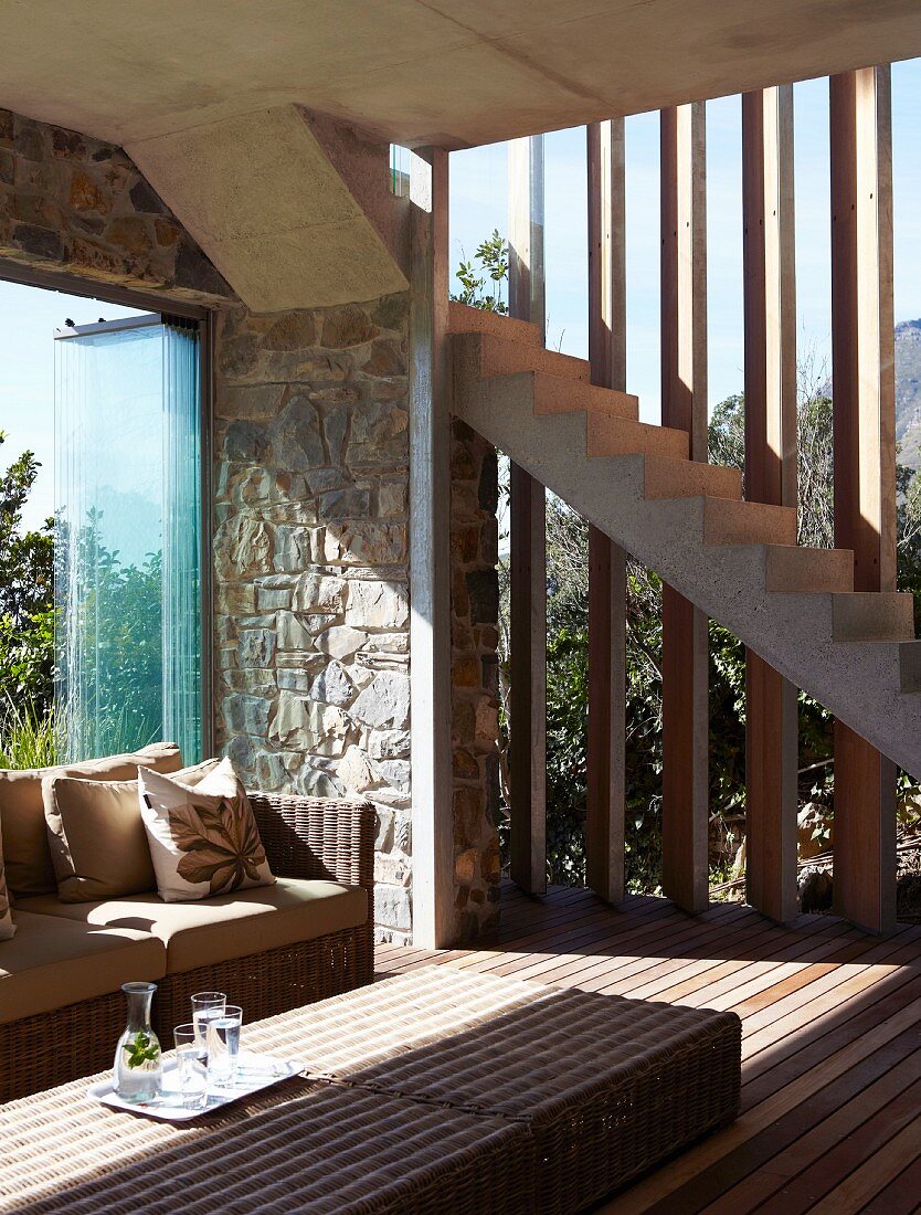 Rattan table and sofa in interior with frameless sliding windows and adjustable wooden sunshade louvers