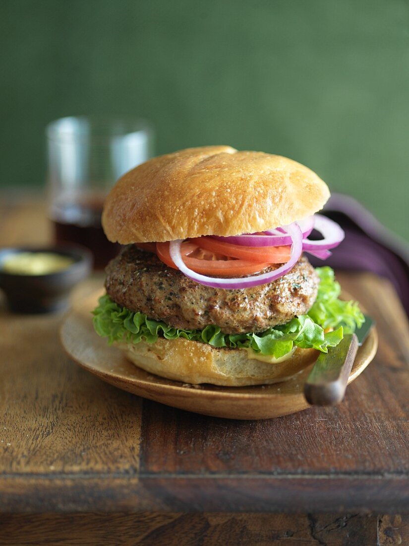 Hamburger with Lettuce, Tomato and Onion on a Plate; On a Wooden Table