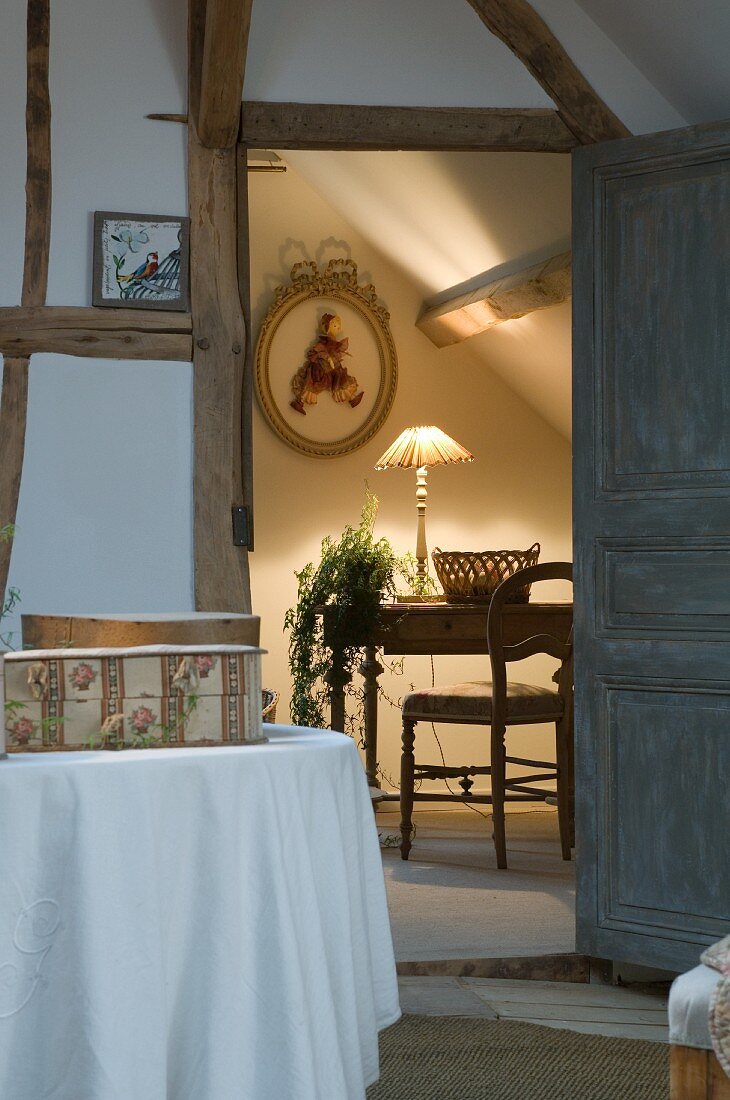 View into cosy, attic chamber with chair and lit table lamp and attractive houseplant on antique table