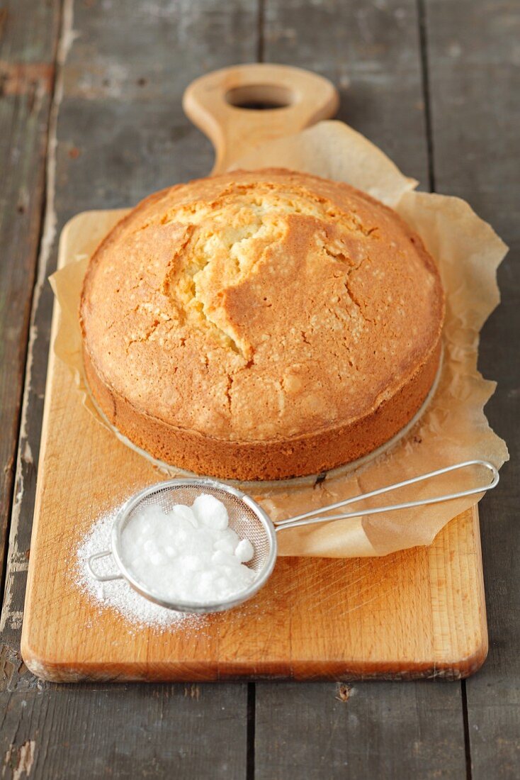 A whole lemon cake and a small sieve with icing sugar