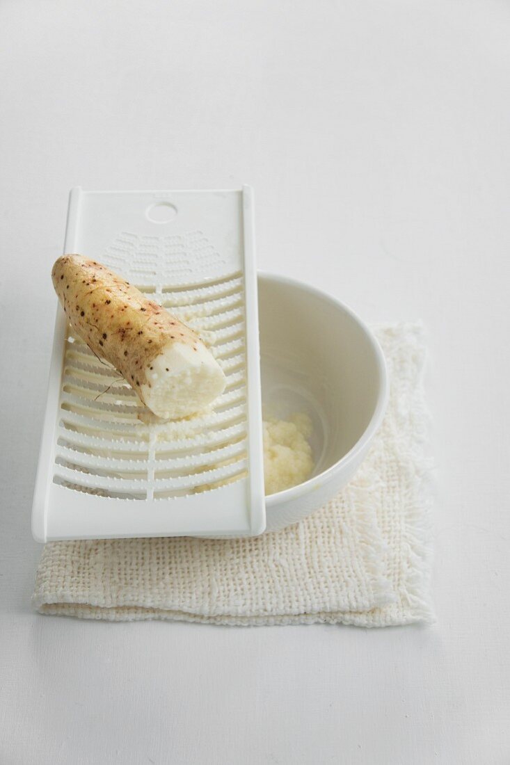 Horseradish on a grater and a bowl of grated horseradish
