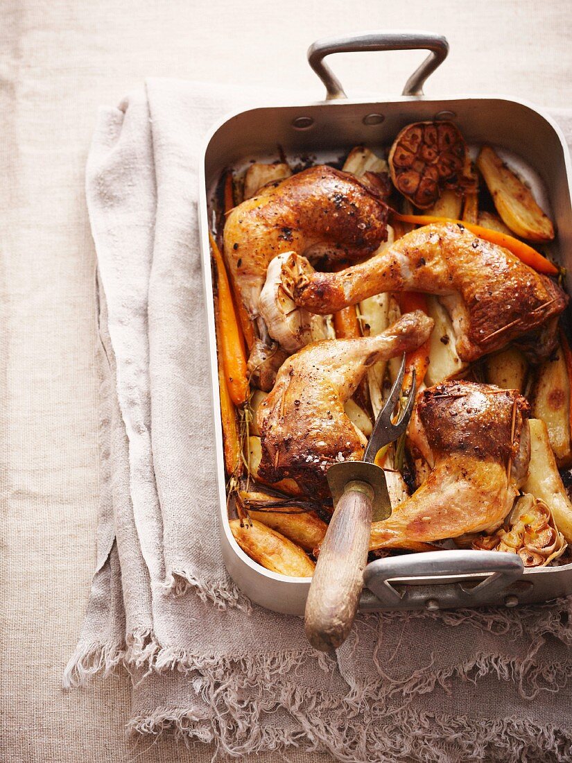 Roast chicken legs on a bed of oven-roasted vegetables in a roasting tin