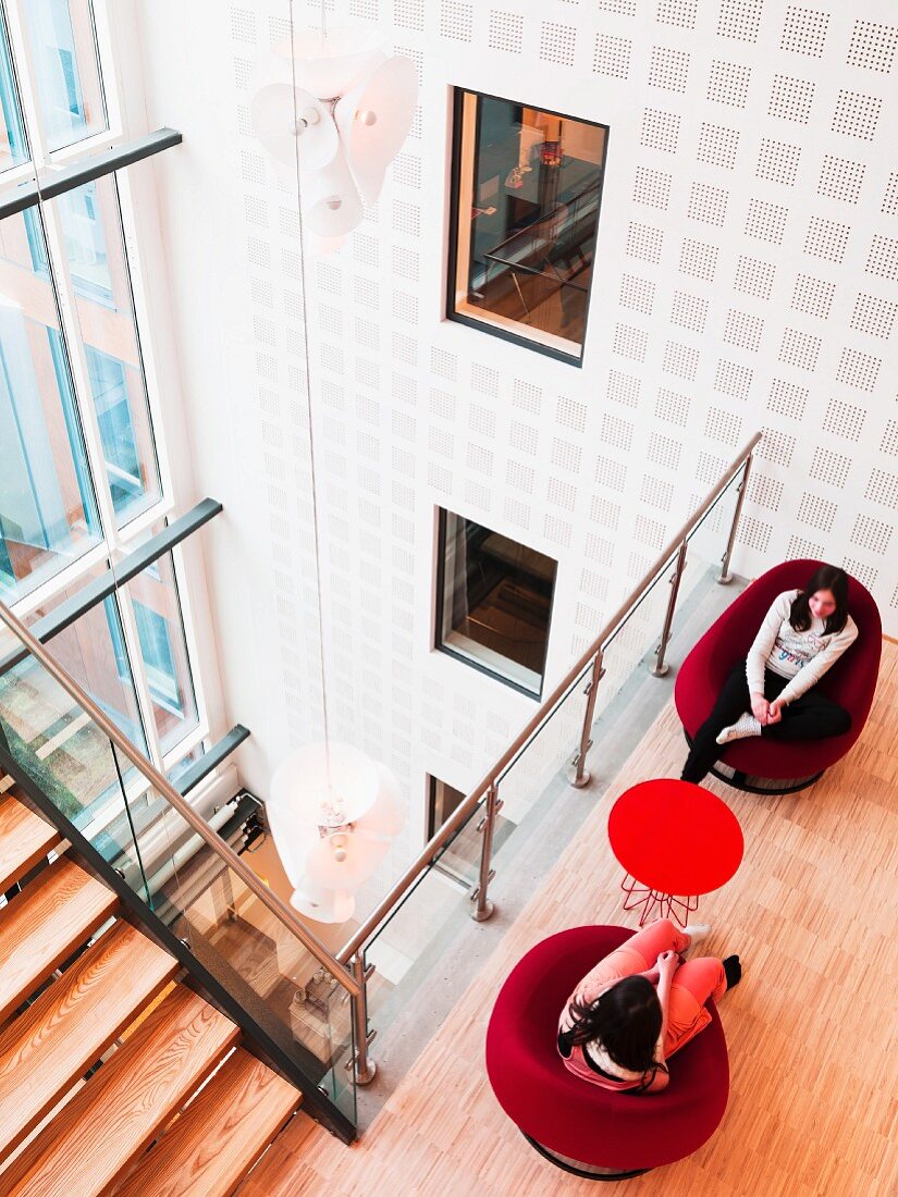 View down onto women sitting on lounge armchairs on gallery next to open space in contemporary building