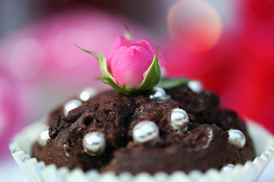 A chocolate muffin decoration with silver balls and a rose bud
