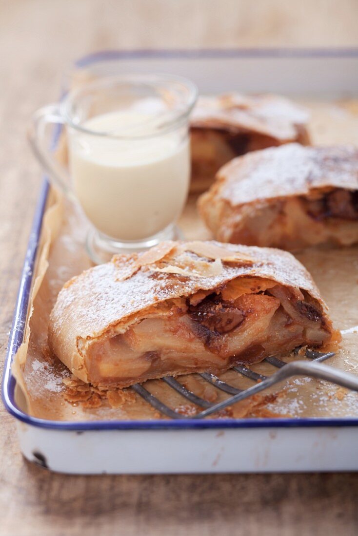 Three slices of pear and quince strudel and a jug of cream on a baking tray