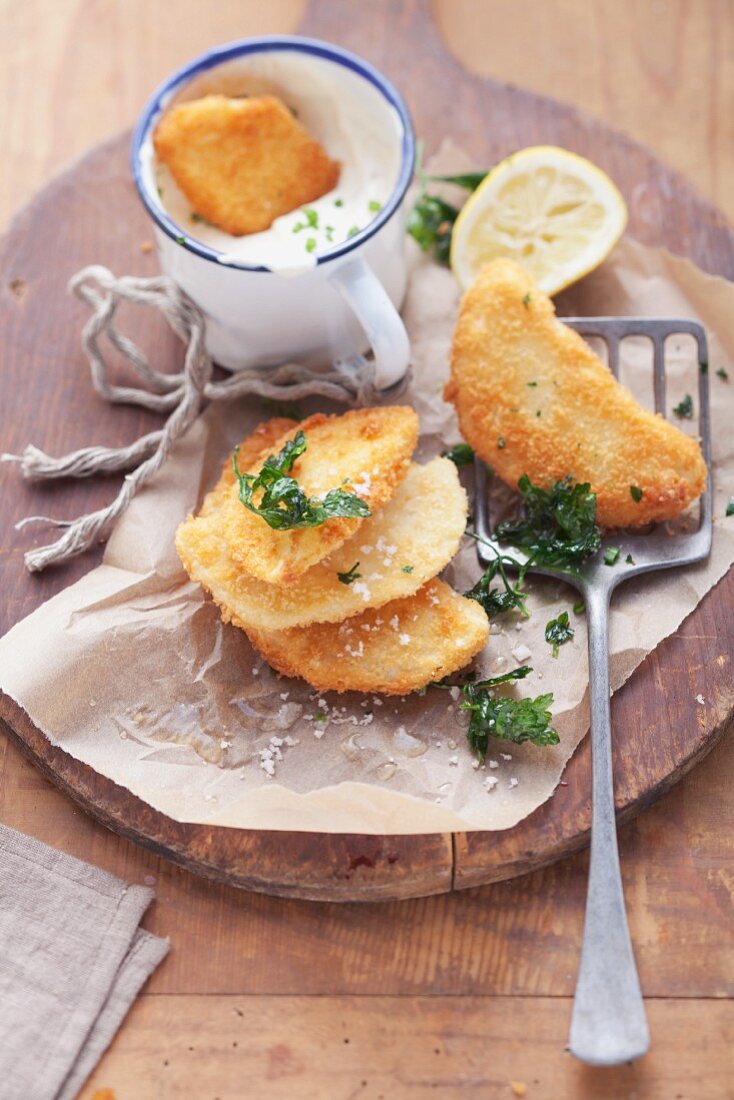 Breaded celery escalopes on baking paper with a spatula with a cup of herb quark in the background