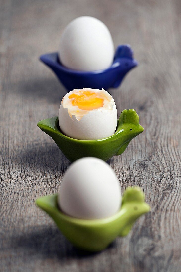 Drei gekochte Eier in Eierbechern, eins davon aufgebrochen