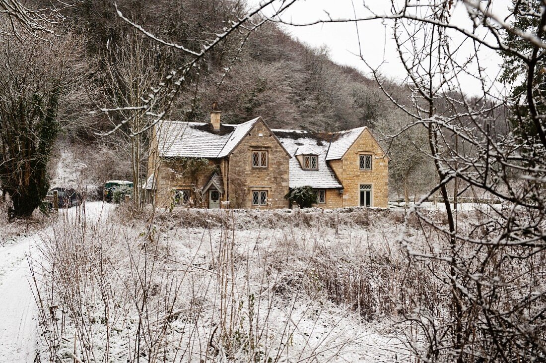 View through bare branches of English country house with brick facade in snowy, winter landscape