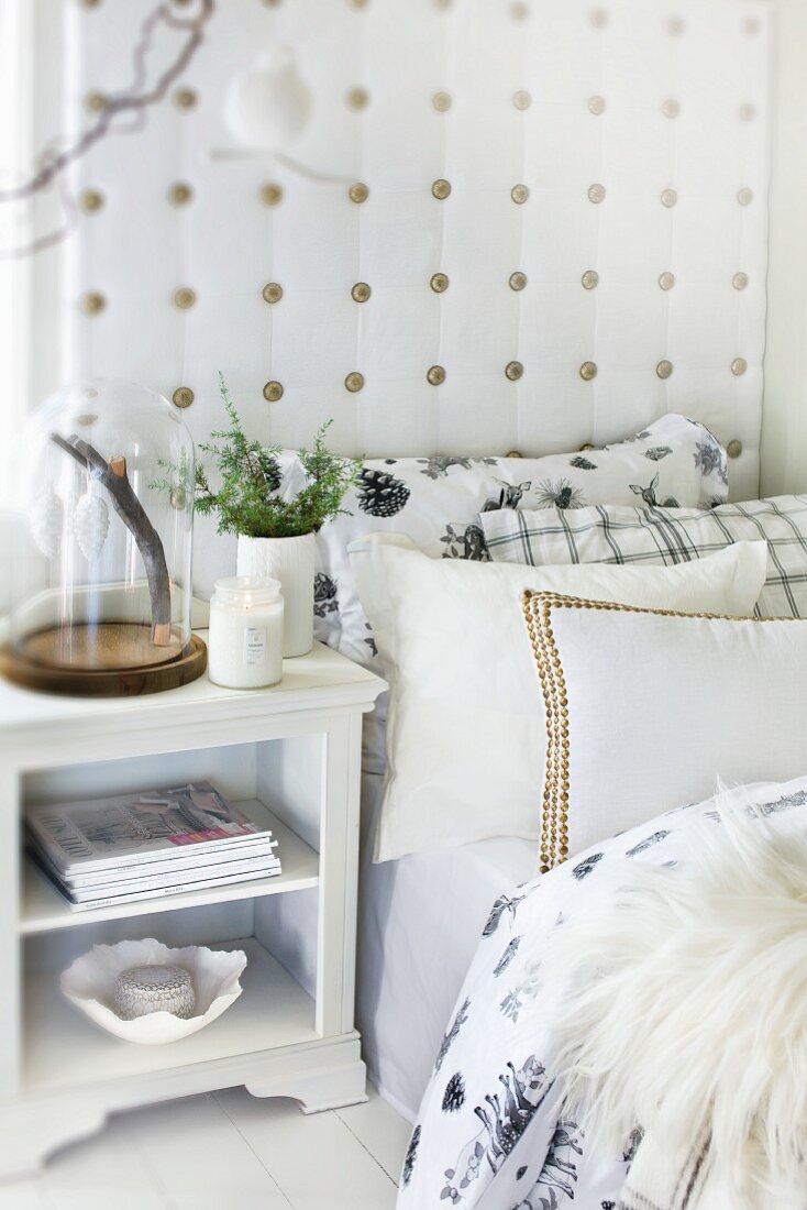 Many scatter cushions on bed with upholstered headboard and bedside cabinet in Scandinavian country-house style